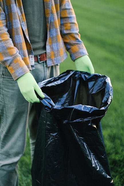 A roadside scene showing a pile of mixed domestic rubbish and waste materials, including black plastic garbage bags, a yellow plastic storage container, and a discarded cushioned armchair with fabric